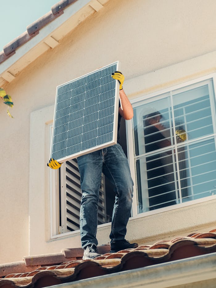 Services Technician carrying a solar panel on a rooftop for installation, promoting renewable energy.